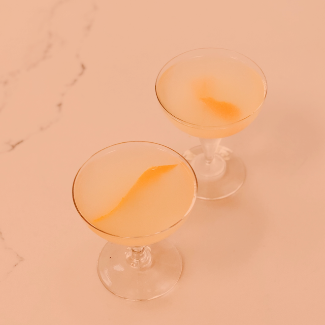 Two cocktail glasses with citrus on a white surface with an orange overlay graphic